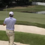 Mira cómo el golpe «bunker» de Scottie Scheffler bounce rebota en un aspersor y acaba rodando hacia el agua